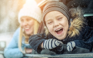 A happy youngster enjoys a Lake George winter drive with a smile on his face as his mother looks on from the back seat.