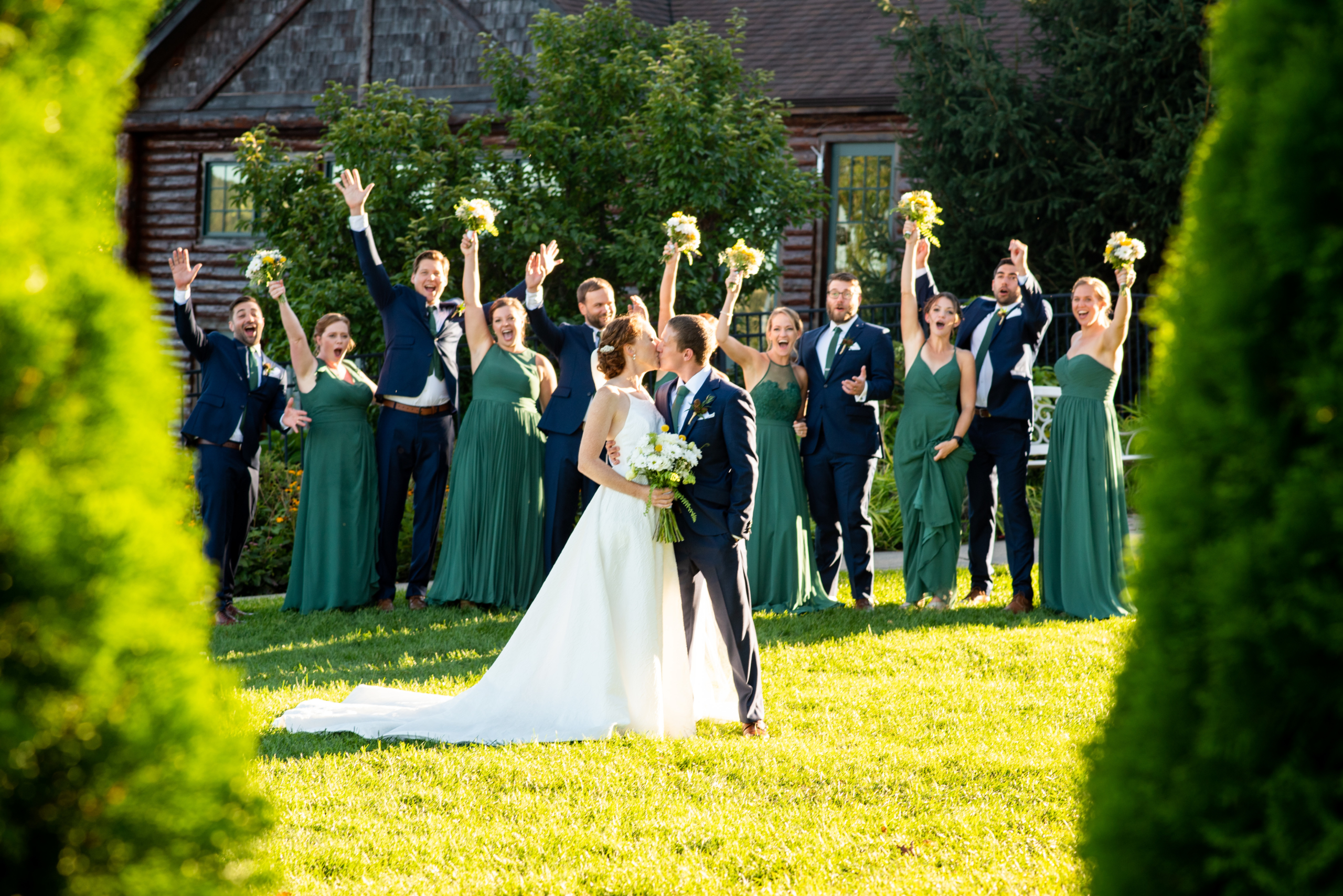 Bride and Groom kissing on lawn. Wedding party cheering